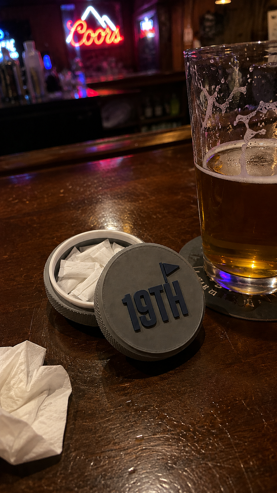 The 19th Hole tin on the bar next to a beer